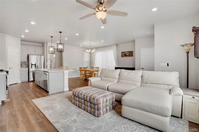 living room with light wood-style floors, ceiling fan with notable chandelier, and recessed lighting