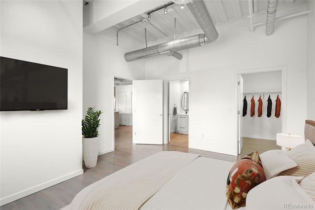 1435 Wazee St Unit 305, Denver, CO 80202 - bedroom featuring a towering ceiling, a spacious closet, baseboards, wood finished floors, and connected bathroom