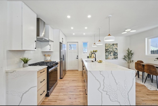 kitchen featuring stainless steel fridge with ice dispenser, light wood-type flooring, range with gas stovetop, wall chimney exhaust hood, and a sink