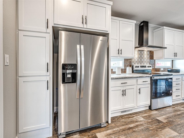 kitchen with dark wood-type flooring, wall chimney exhaust hood, stainless steel appliances, decorative backsplash, and white cabinetry