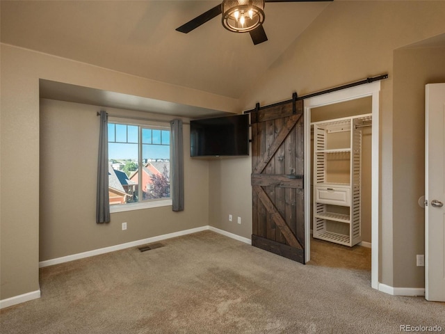 unfurnished bedroom with ceiling fan, a barn door, carpet floors, a closet, and lofted ceiling