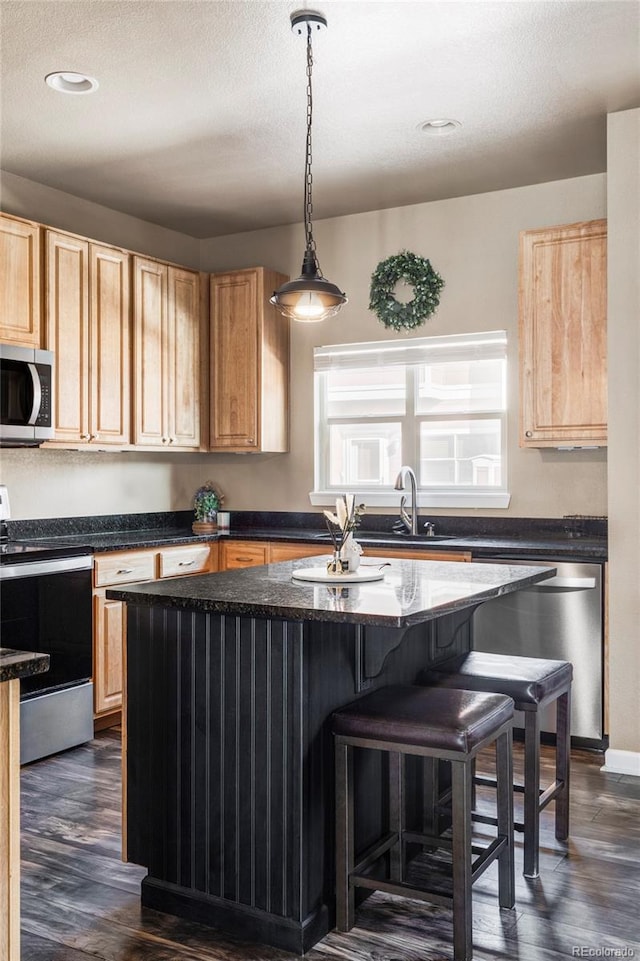 kitchen with hanging light fixtures, dark stone countertops, dark hardwood / wood-style flooring, a kitchen island, and stainless steel appliances