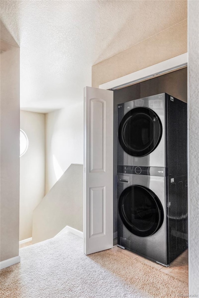 clothes washing area featuring stacked washing maching and dryer, carpet, and a textured ceiling