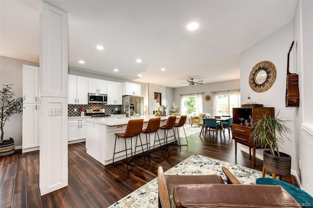 22026 Hill Gail Way, Parker, CO 80138 - kitchen with stainless steel appliances, a center island with sink, dark wood-style floors, light countertops, and decorative backsplash
