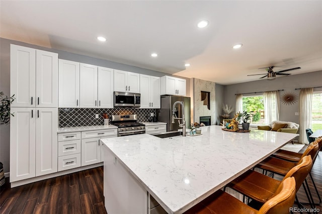 22026 Hill Gail Way, Parker, CO 80138 - kitchen with appliances with stainless steel finishes, a kitchen bar, dark wood-style flooring, a large island, and tasteful backsplash