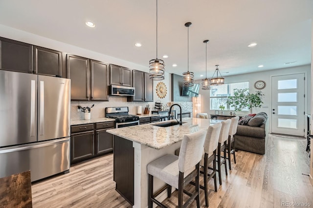 kitchen featuring a kitchen bar, a sink, stainless steel appliances, light stone countertops, and light wood-style floors