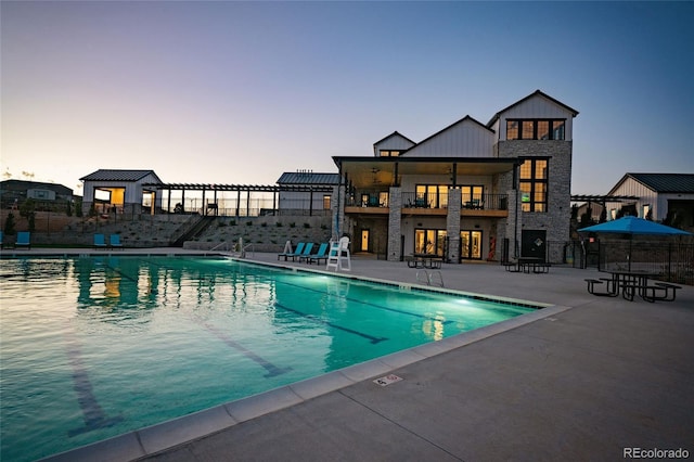 pool at dusk with a patio area, fence, and a community pool