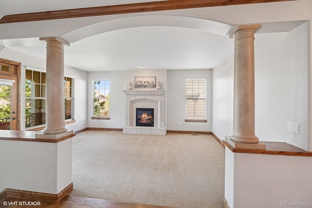 unfurnished living room with a healthy amount of sunlight, carpet flooring, baseboards, and decorative columns