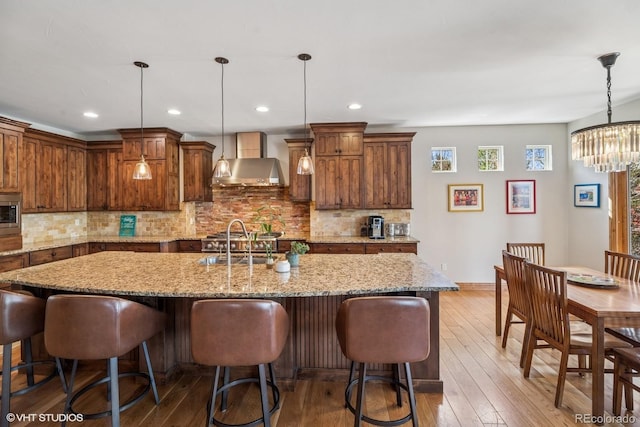 kitchen featuring a kitchen bar, wall chimney range hood, hardwood / wood-style flooring, and a kitchen island with sink