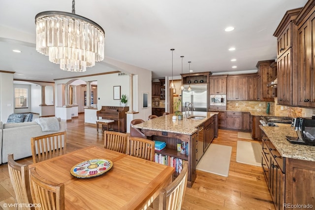 dining area featuring arched walkways, light wood finished floors, recessed lighting, and decorative columns