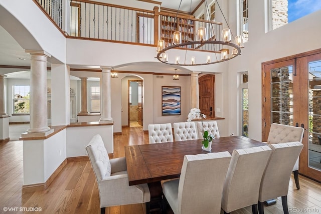 dining room featuring decorative columns, a towering ceiling, arched walkways, and light wood-style floors