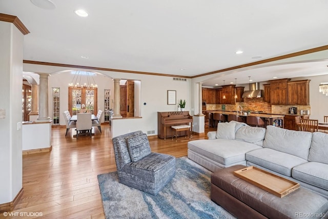 living room with light wood-style floors, arched walkways, an inviting chandelier, visible vents, and decorative columns