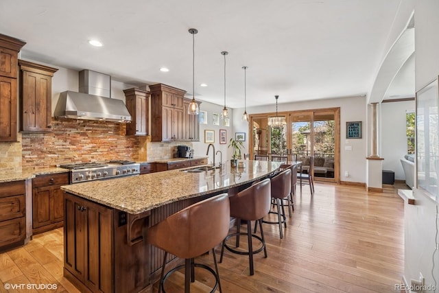 kitchen with tasteful backsplash, wall chimney exhaust hood, light wood-type flooring, and a sink