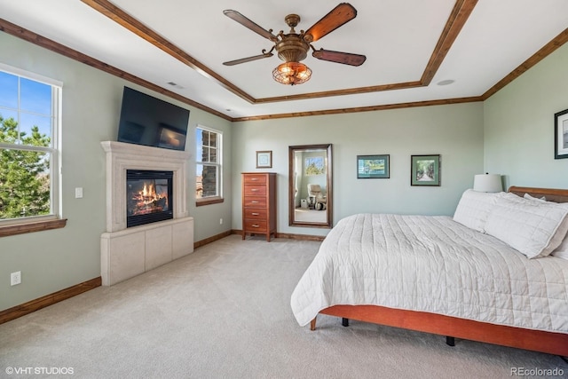 bedroom with light carpet, a tray ceiling, a glass covered fireplace, and crown molding