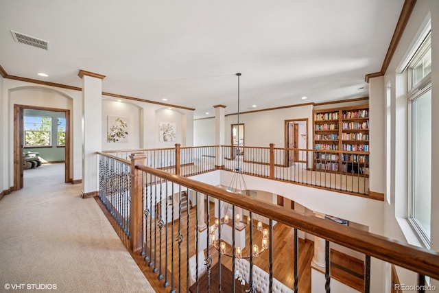 hallway featuring visible vents, ornamental molding, and an upstairs landing