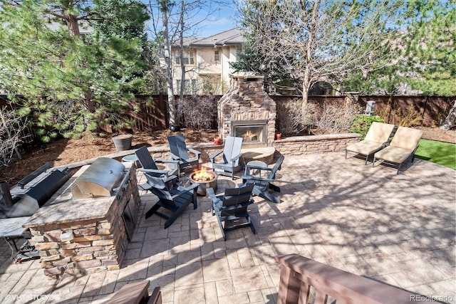 view of patio / terrace with exterior kitchen, an outdoor stone fireplace, a fenced backyard, and a fire pit