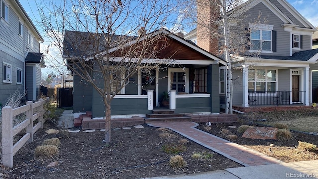 view of front of house with a porch, a chimney, roof with shingles, and fence