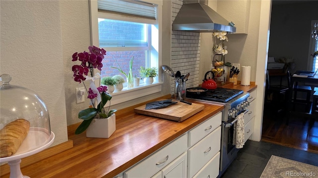 kitchen with high end stove, butcher block countertops, white cabinetry, extractor fan, and a textured wall