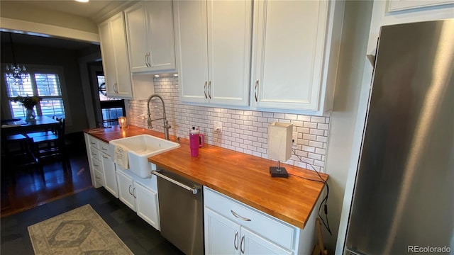 kitchen featuring decorative backsplash, white cabinets, stainless steel appliances, wood counters, and a sink