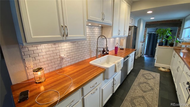 kitchen with a sink, decorative backsplash, white cabinets, and wood counters