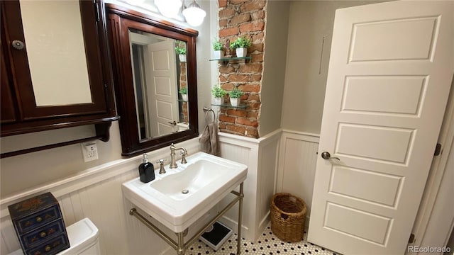 half bath with wainscoting, toilet, and a sink