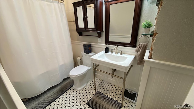 full bathroom featuring curtained shower, toilet, and wainscoting