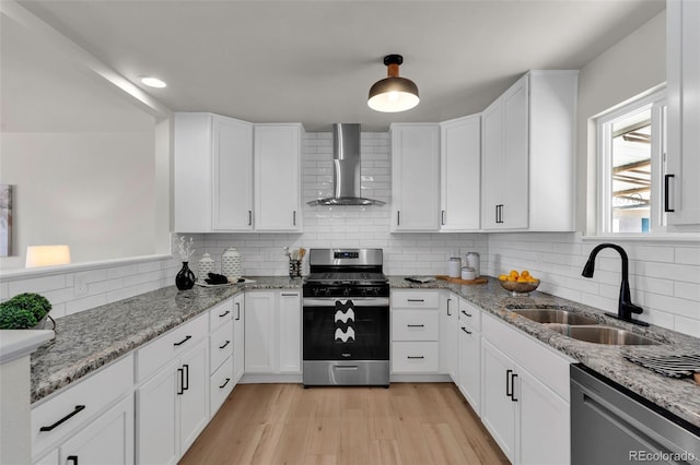 kitchen featuring light stone counters, white cabinets, stainless steel appliances, and wall chimney range hood