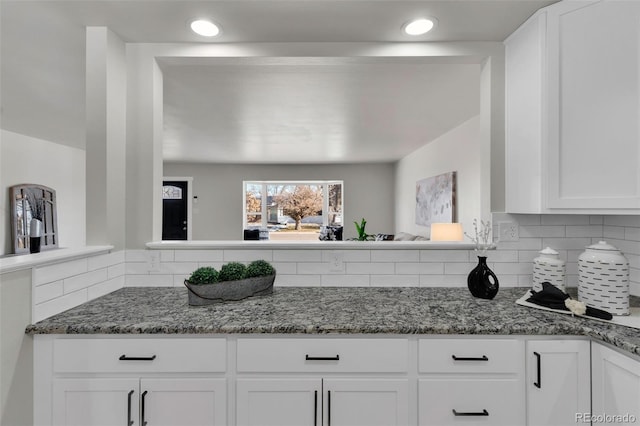 kitchen with dark stone countertops, white cabinets, and backsplash