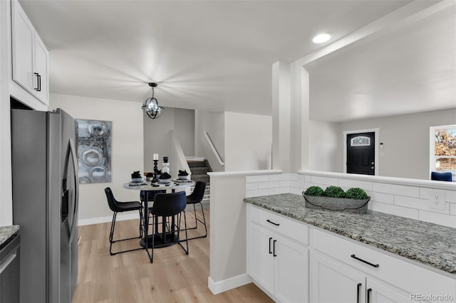 kitchen with pendant lighting, stainless steel fridge, white cabinetry, light stone counters, and light wood-type flooring