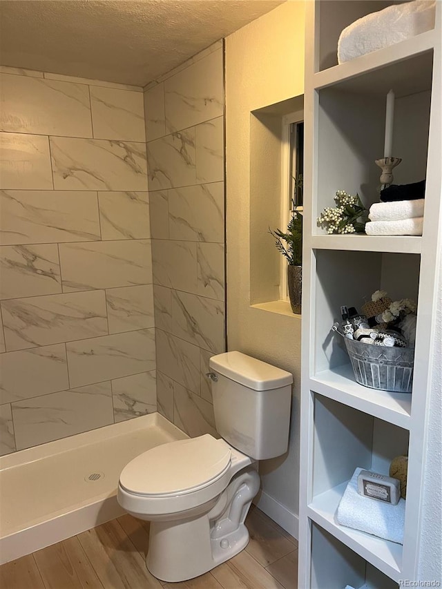 bathroom with hardwood / wood-style flooring, a textured ceiling, toilet, and tiled shower