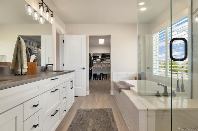 bathroom with a spacious closet, wood finished floors, double vanity, and a garden tub