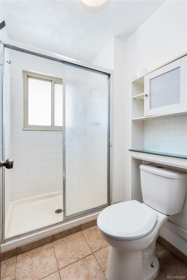 bathroom with a shower with door, tile patterned floors, backsplash, and toilet