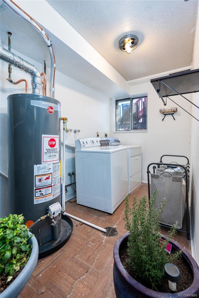 washroom featuring washing machine and dryer, water heater, and a textured ceiling