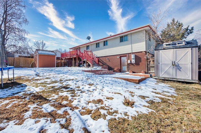 snow covered back of property featuring a wooden deck, a trampoline, and a shed