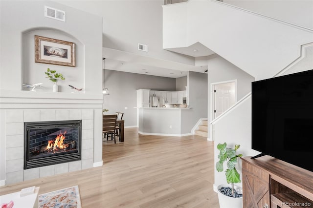 living room featuring a high ceiling, light wood-type flooring, and a fireplace