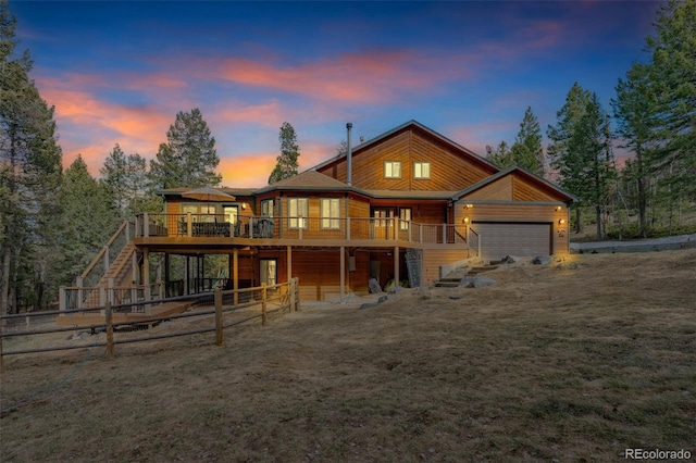 back of property at dusk with stairway, a wooden deck, fence, and a garage