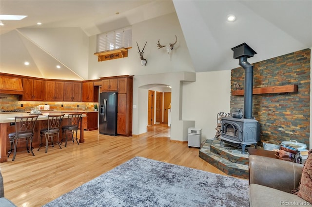living room with high vaulted ceiling, a skylight, light wood-type flooring, arched walkways, and a wood stove