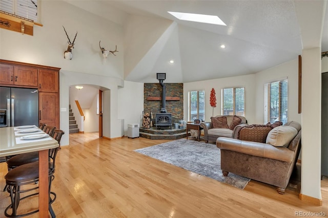 living room with stairway, a wood stove, arched walkways, light wood-style flooring, and high vaulted ceiling