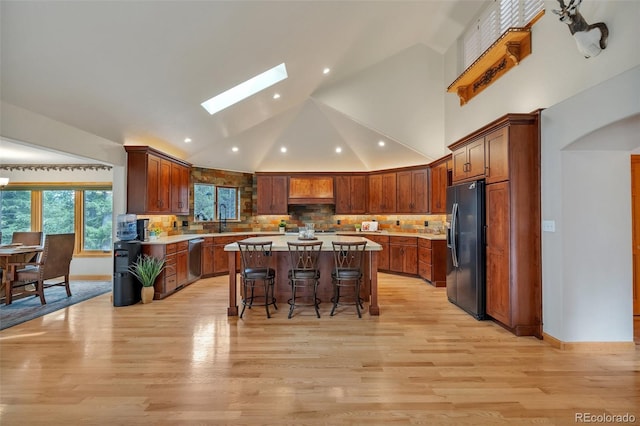 kitchen with stainless steel dishwasher, a center island, a kitchen breakfast bar, a skylight, and black fridge with ice dispenser