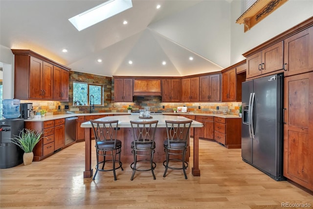 kitchen with a kitchen breakfast bar, a skylight, light wood-type flooring, appliances with stainless steel finishes, and a kitchen island