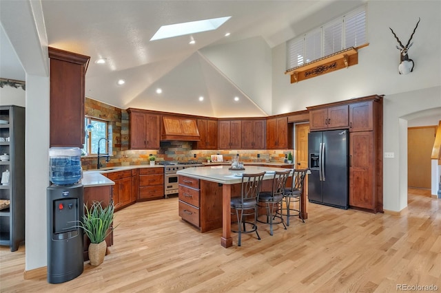 kitchen with a kitchen island, a skylight, high end range, custom exhaust hood, and black fridge