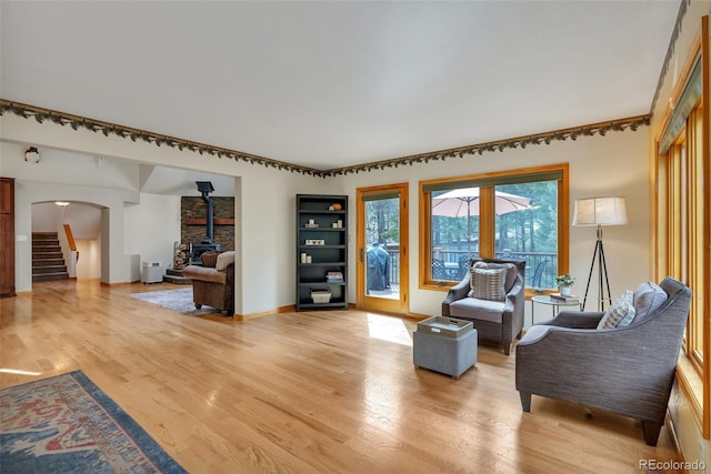 living room featuring a wood stove, arched walkways, light wood-type flooring, baseboards, and stairs