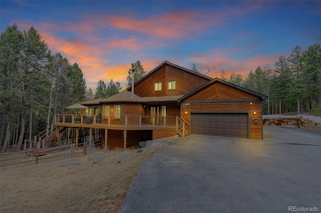 chalet / cabin featuring a wooden deck, an attached garage, stairs, and aphalt driveway