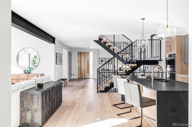 kitchen with sink, stainless steel double oven, pendant lighting, light hardwood / wood-style floors, and a kitchen bar