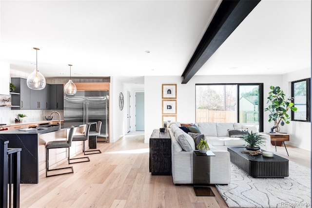 living room featuring beamed ceiling, light wood-type flooring, and sink