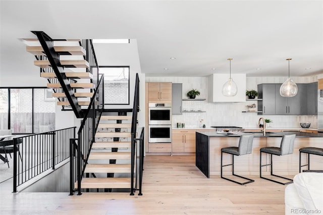 kitchen featuring gray cabinetry, a breakfast bar, stainless steel double oven, pendant lighting, and light hardwood / wood-style flooring