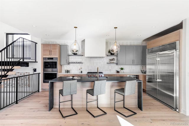 kitchen featuring stainless steel appliances, a center island with sink, light hardwood / wood-style floors, hanging light fixtures, and a breakfast bar area