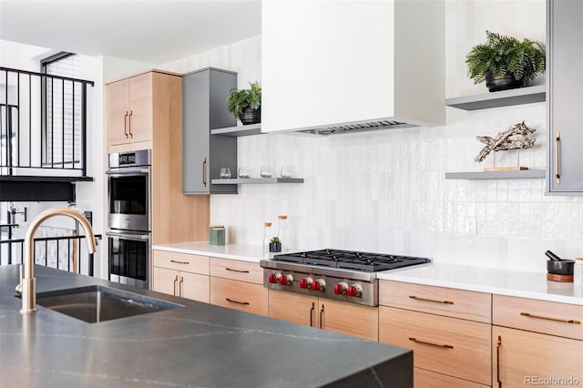 kitchen with ventilation hood, sink, decorative backsplash, light brown cabinetry, and appliances with stainless steel finishes