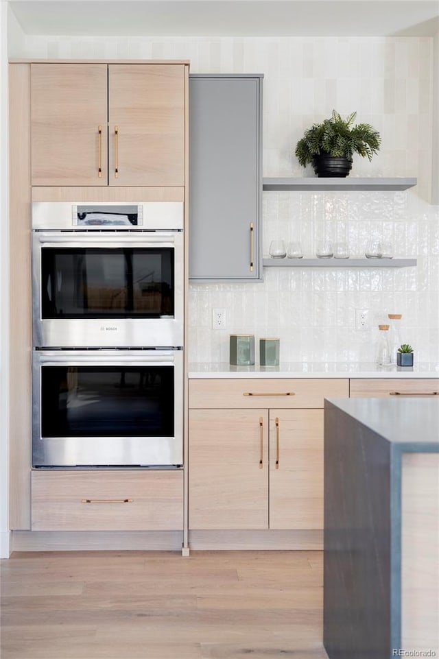 kitchen featuring decorative backsplash, light brown cabinets, stainless steel double oven, and light hardwood / wood-style flooring