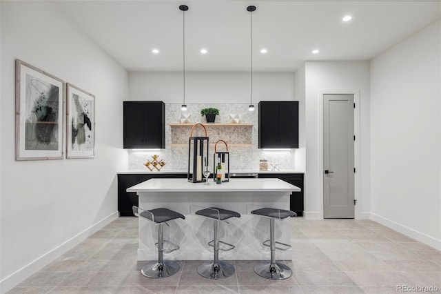 kitchen with decorative backsplash, a kitchen breakfast bar, light tile patterned floors, a center island with sink, and hanging light fixtures